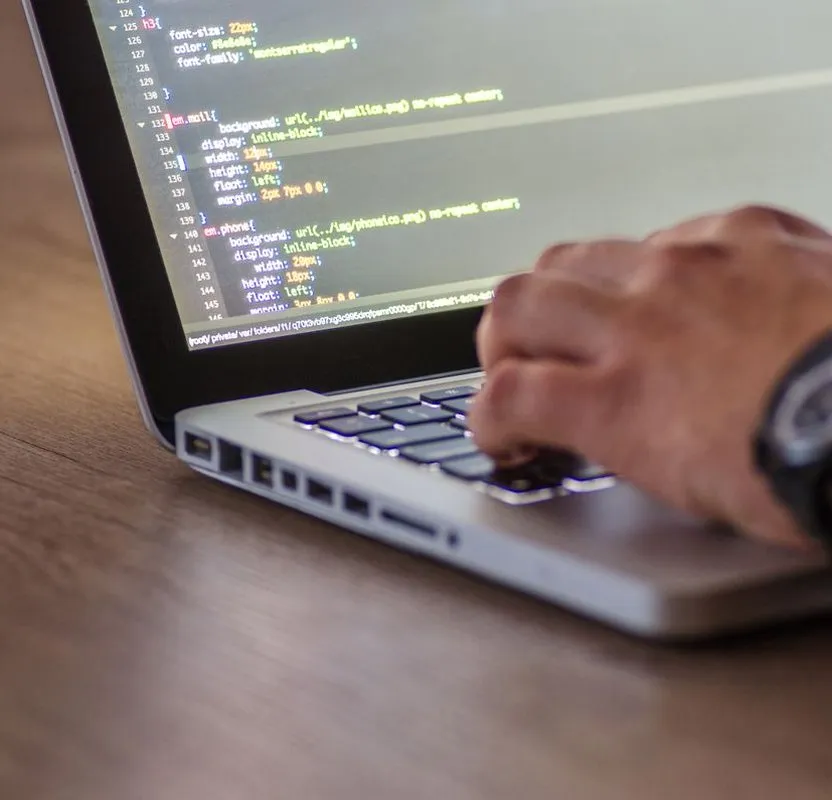 Close-up of a hand typing code on a laptop during website development