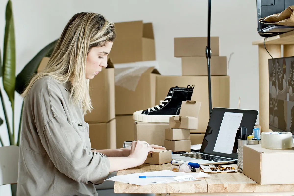 A shopkeeper preparing an online order next to a laptop and packaging boxes